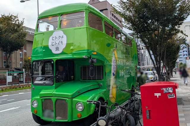 正面から見た綾鷹『ヒトクチヒトイキ旅』2階建てコラボバス。深緑の車体とロゴが印象的。