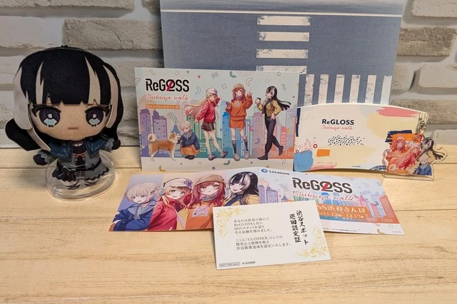 ReGLOSS渋谷さんぽで獲得したポストカードや巡回認定証などのアイテムを並べ、らでんちゃんのホロフレと一緒に記念撮影した写真。イベントの達成感が伝わるショット
