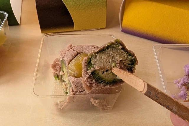 和菓子・実りを一口サイズにカットし、串で持ち上げたところ。黄色い栗あんと抹茶あんの層がきれいに見える。